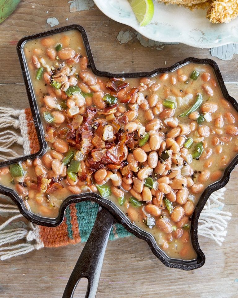 black pepper and bacon pinto beans in a cast iron skillet shaped like texas