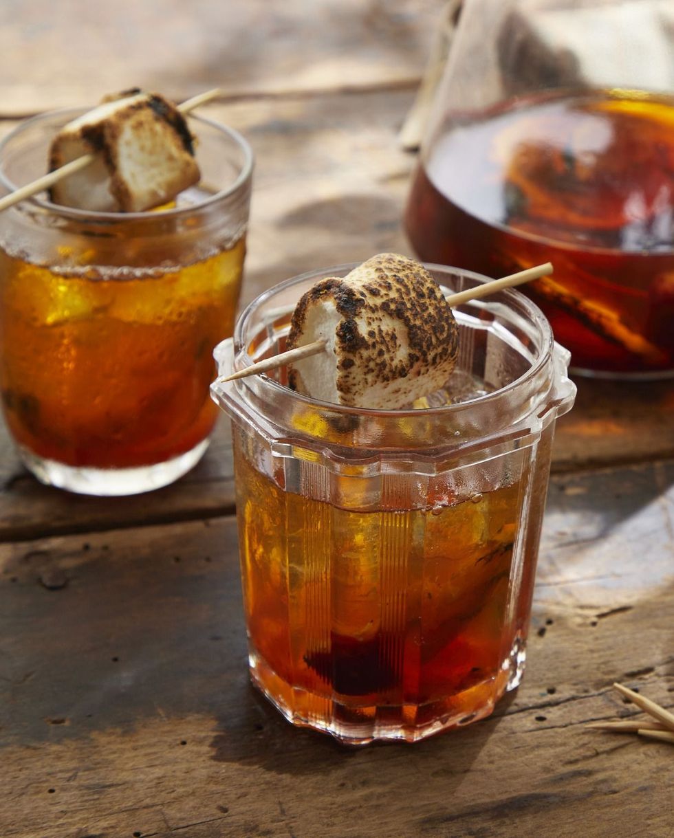 grilled orange old fashioned in a jar with grilled orange and ice and garnished with a toasted marshmallow on a toothpick
